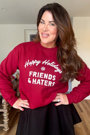 Emily Simpson wearing a red crewneck sweatshirt with "Happy Holidays Friends & Haters" printed on middle front of sweatshirt in white writing. 