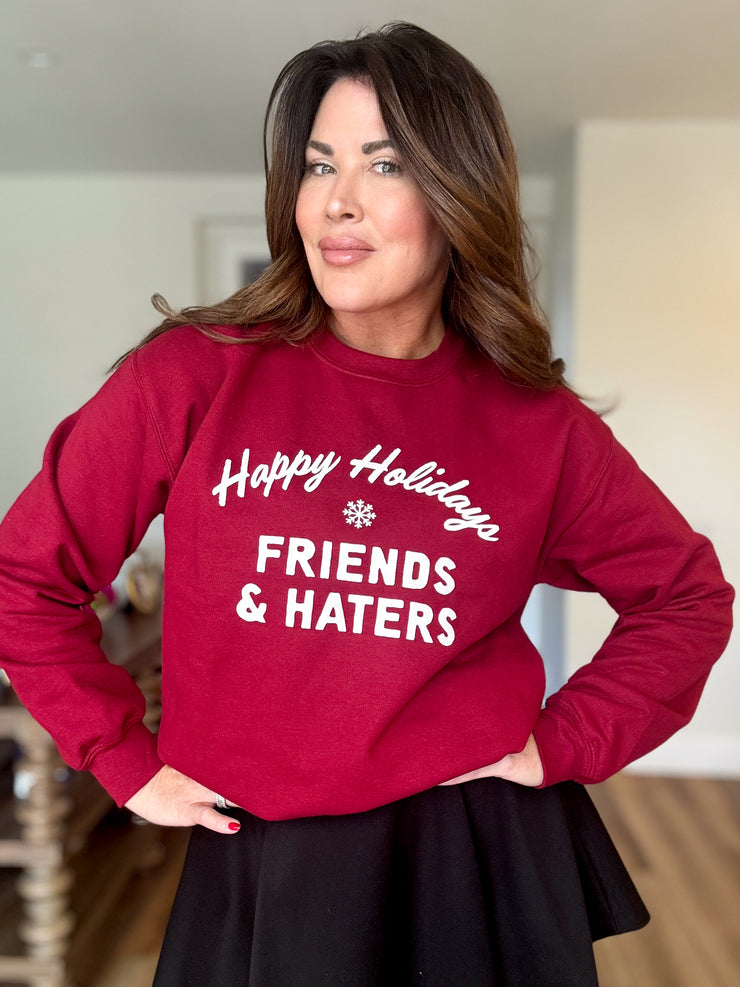 Emily Simpson wearing a red crewneck sweatshirt with "Happy Holidays Friends & Haters" printed on middle front of sweatshirt in white writing. 