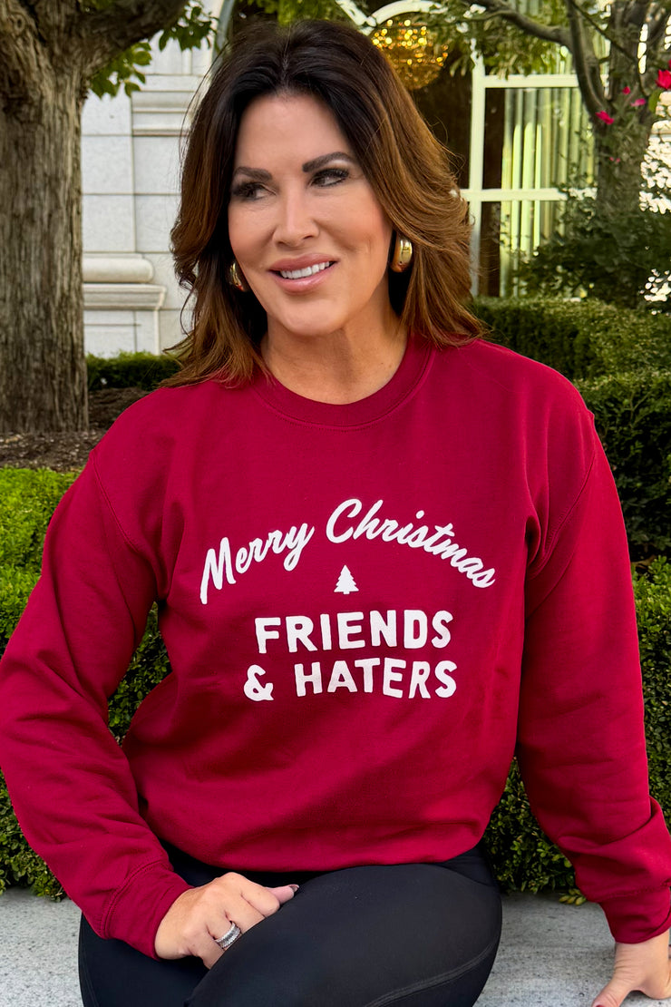 Emily Simpson wearing a red crewneck sweatshirt with "Merry Christmas Friends & Haters" printed on middle front of sweatshirt in white writing. 