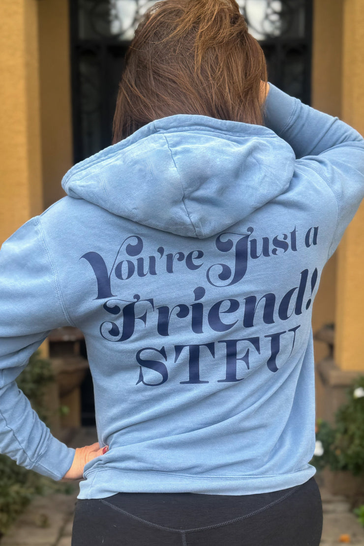 Emily Simpson wearing a blue hoodie with the words You're Just a Friend STFU printed in large font covering the width of the back of the hoodie in blue.